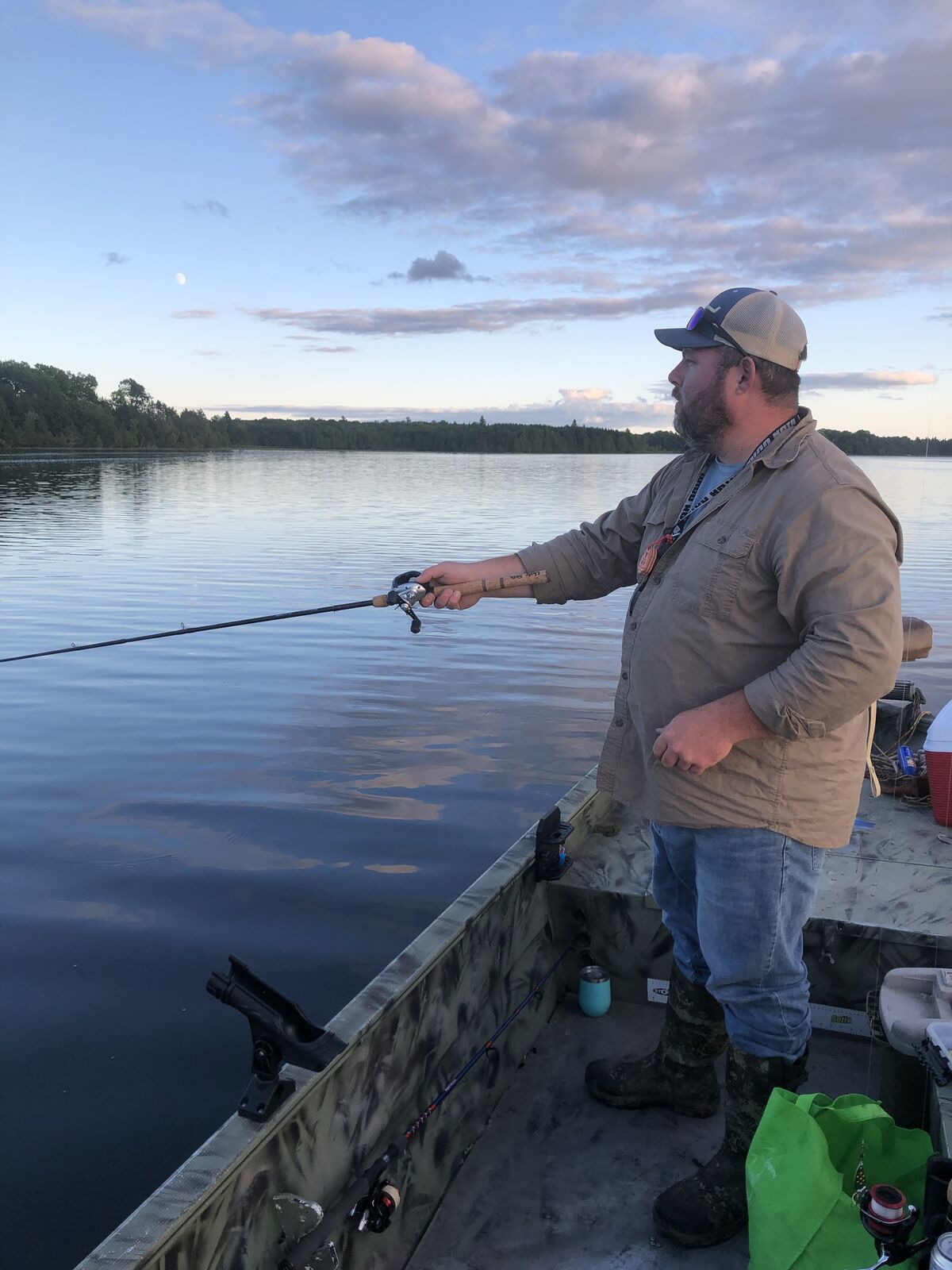 Ryan casting a fishing line from a boat on a calm lake at dusk.