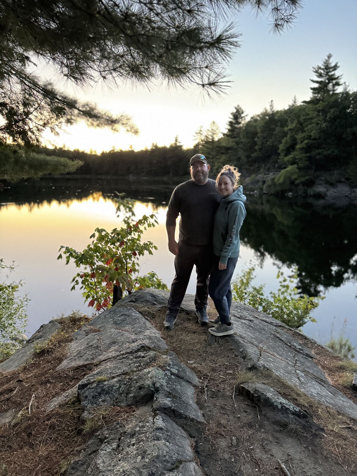 Ryan and Tausha standing together on a rock outcrop at sunset overlooking a lake in Lanark Highlands.